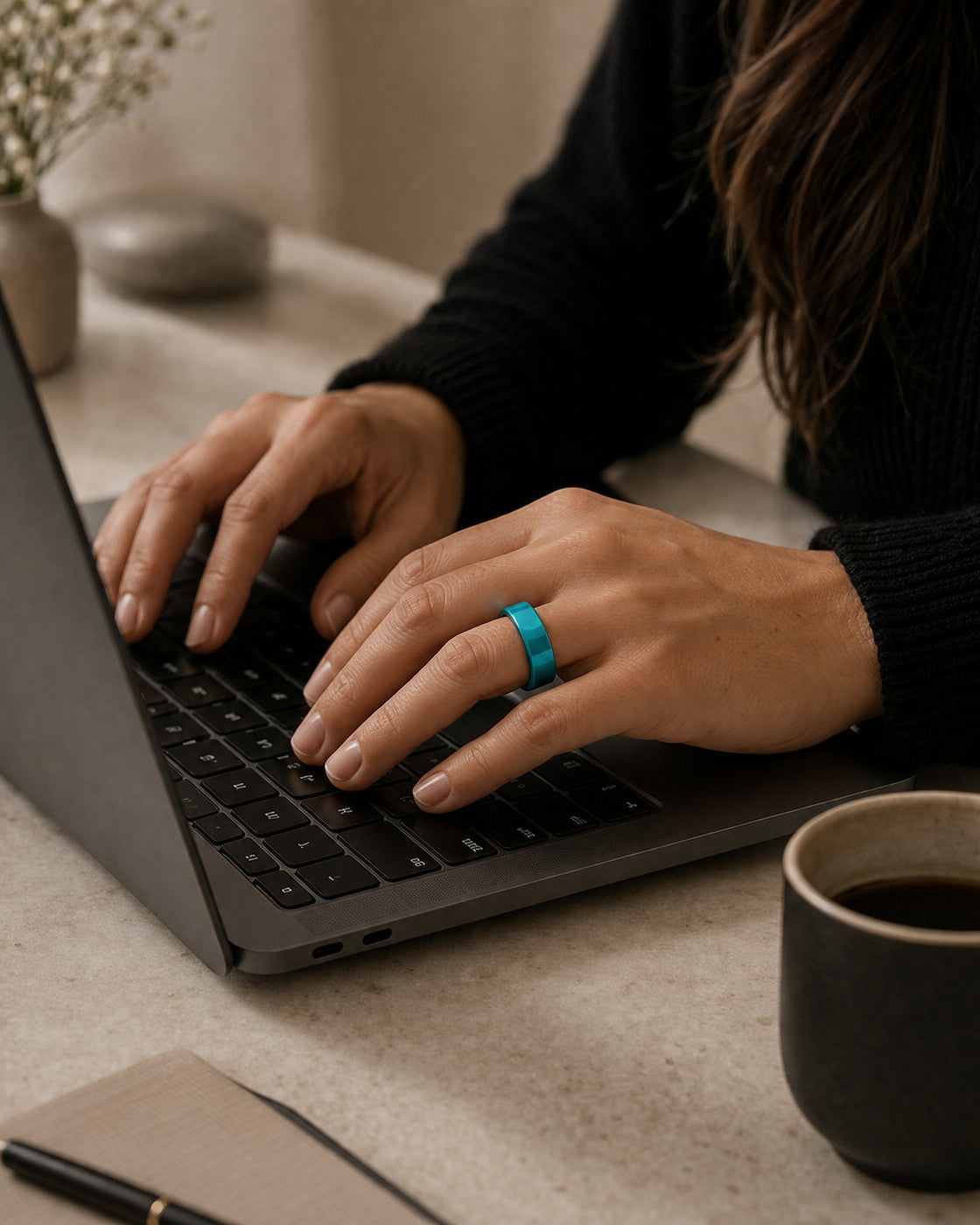 Woman wearing the Kayza PRO teal smart ring while typing at a laptop