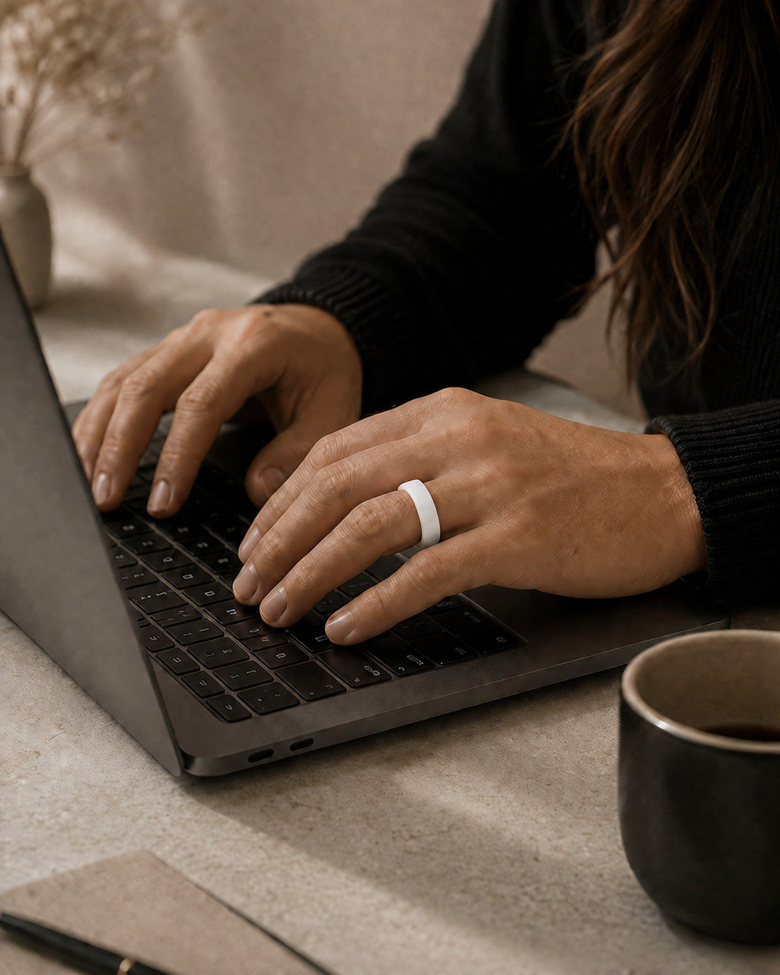 Woman wearing the Kayza PRO white smart ring while typing at a laptop